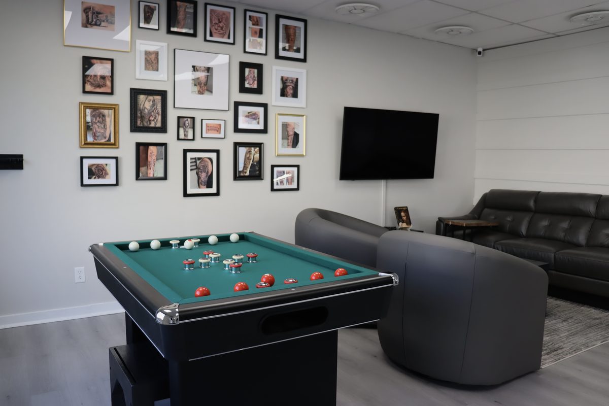 The lounge: bumper pool table, leather seating, TV, and a gallery wall of framed portfolio work
