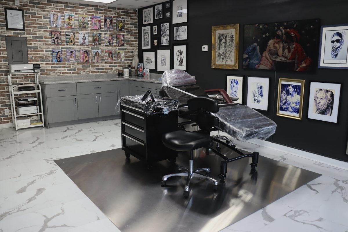 The tattoo studio: brick wall with vintage magazines, dark gallery wall with original artwork, marble floors, professional workstation